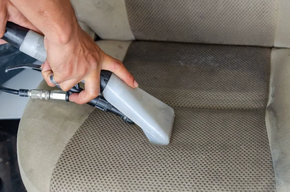 Detailer deep-cleaning a car seat with a vacuum extractor