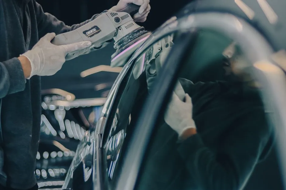 Machine polisher buffing a car's dark paintwork to a high-gloss finish